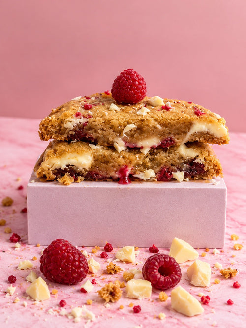 Cookie framboises chocolat blanc coupé en deux sur fond rose